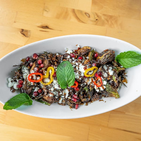 Roasted Brussels sprouts with feta, pomegranate seeds, peppers, and mint in a white dish.