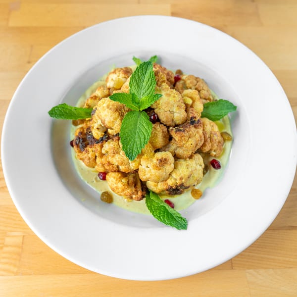 Roasted cauliflower florets with mint, pomegranate seeds, and golden raisins on a creamy green sauce.