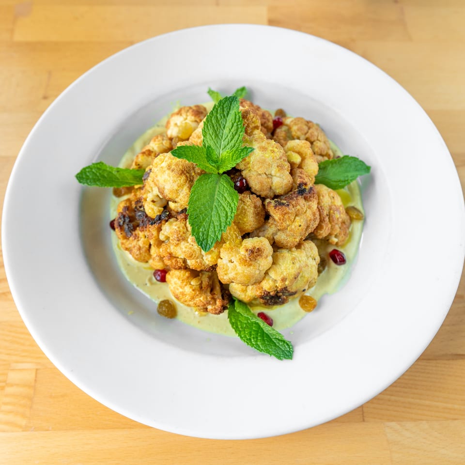 Roasted cauliflower florets with mint, pomegranate seeds, and golden raisins on a creamy green sauce.