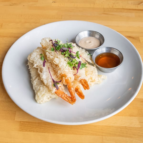Crispy tempura shrimp garnished with microgreens, served with two dipping sauces on a white plate.