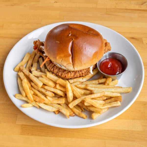 Crispy chicken sandwich with coleslaw and a side of golden french fries and ketchup on a white plate.
